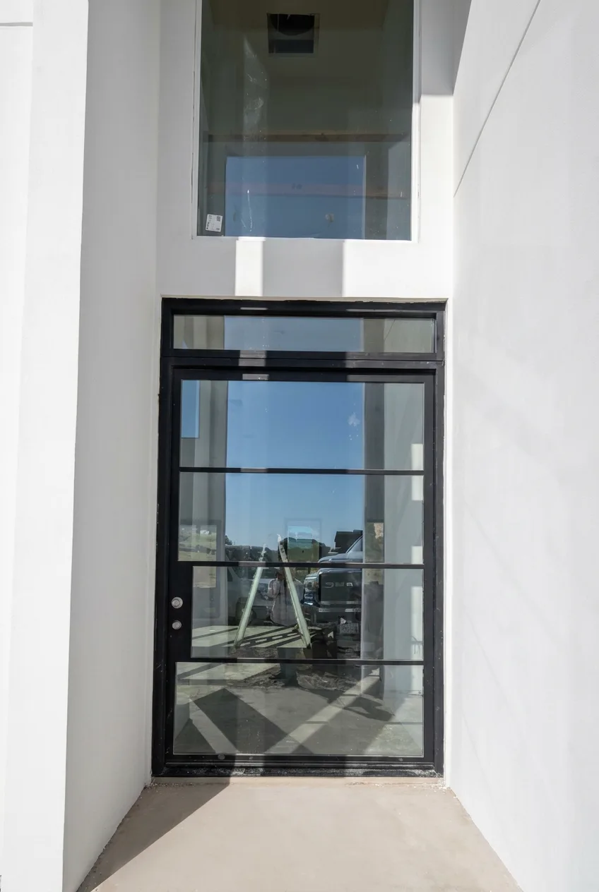 Black-framed glass entry door with transom in a white stucco entry